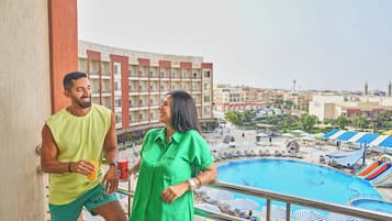 A balcony with a view of a swimming pool, lounge chairs, umbrellas, and a hotel building in the background.