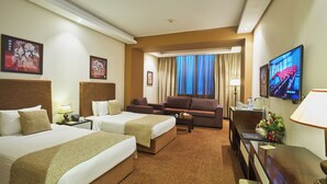Habitación de hotel con dos camas, un sofá, un televisor y un escritorio con lámpara.