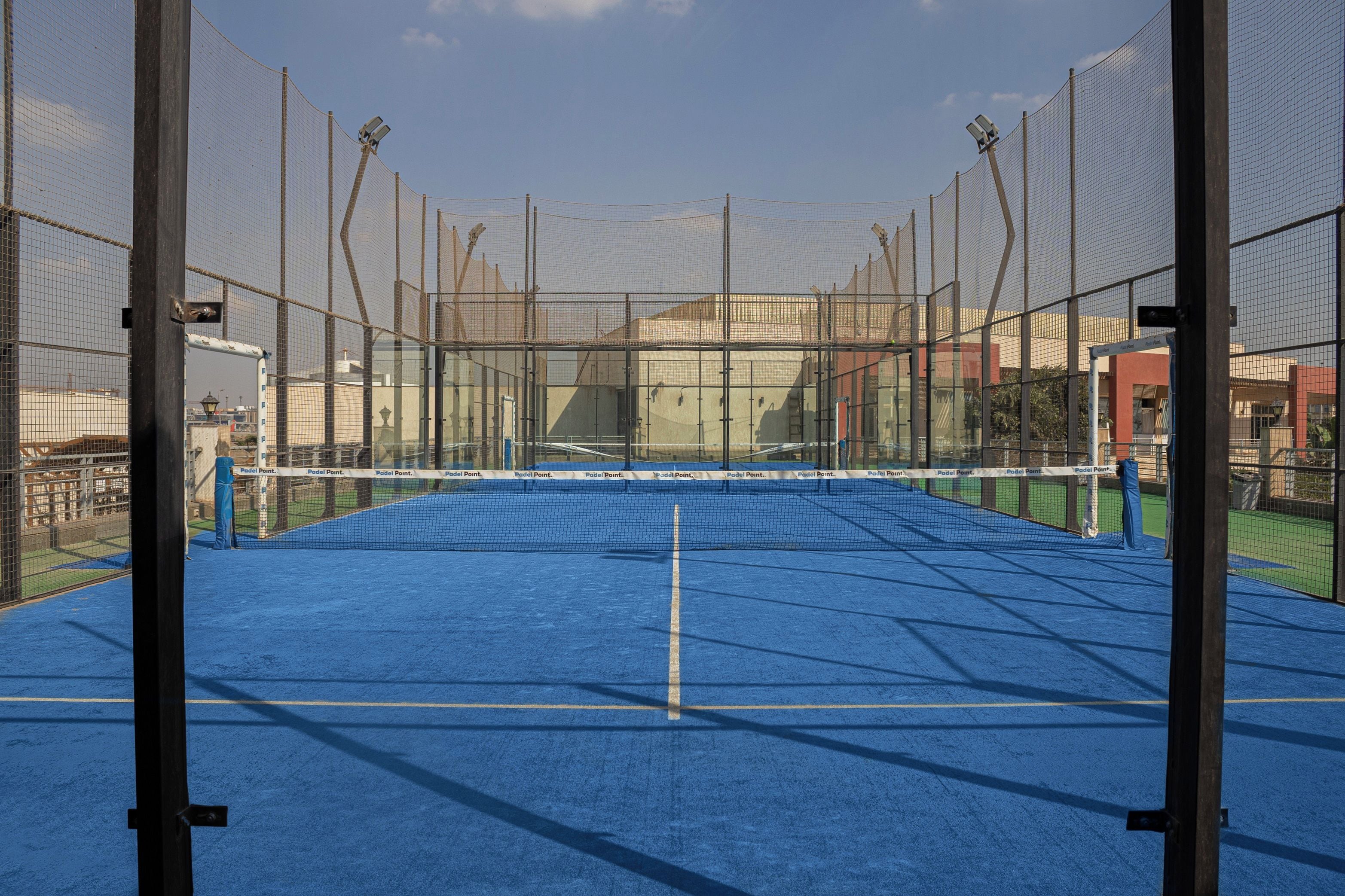 Una cancha de tenis con red, rodeada por una valla, y un edificio al fondo.