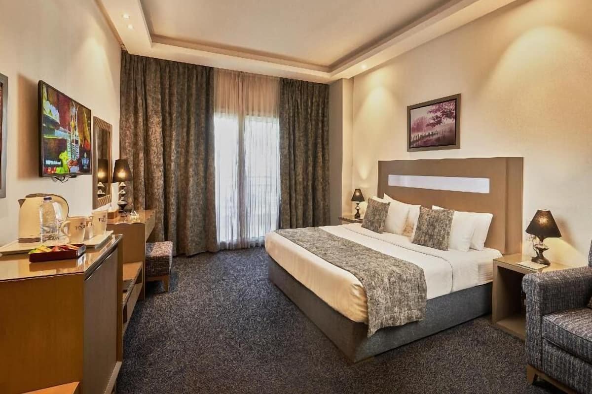 Habitación de hotel con cama, escritorio, silla, mesita de noche y ventana con cortinas.