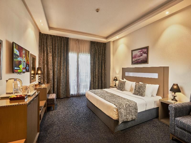 Habitación de hotel con cama, escritorio, silla, mesita de noche y ventana con cortinas.