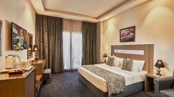 Habitación de hotel con cama, escritorio, silla, mesita de noche y ventana con cortinas.