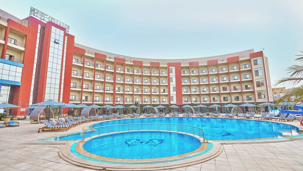 Un hotel con una piscina amplia, varios balcones y sillas de descanso.