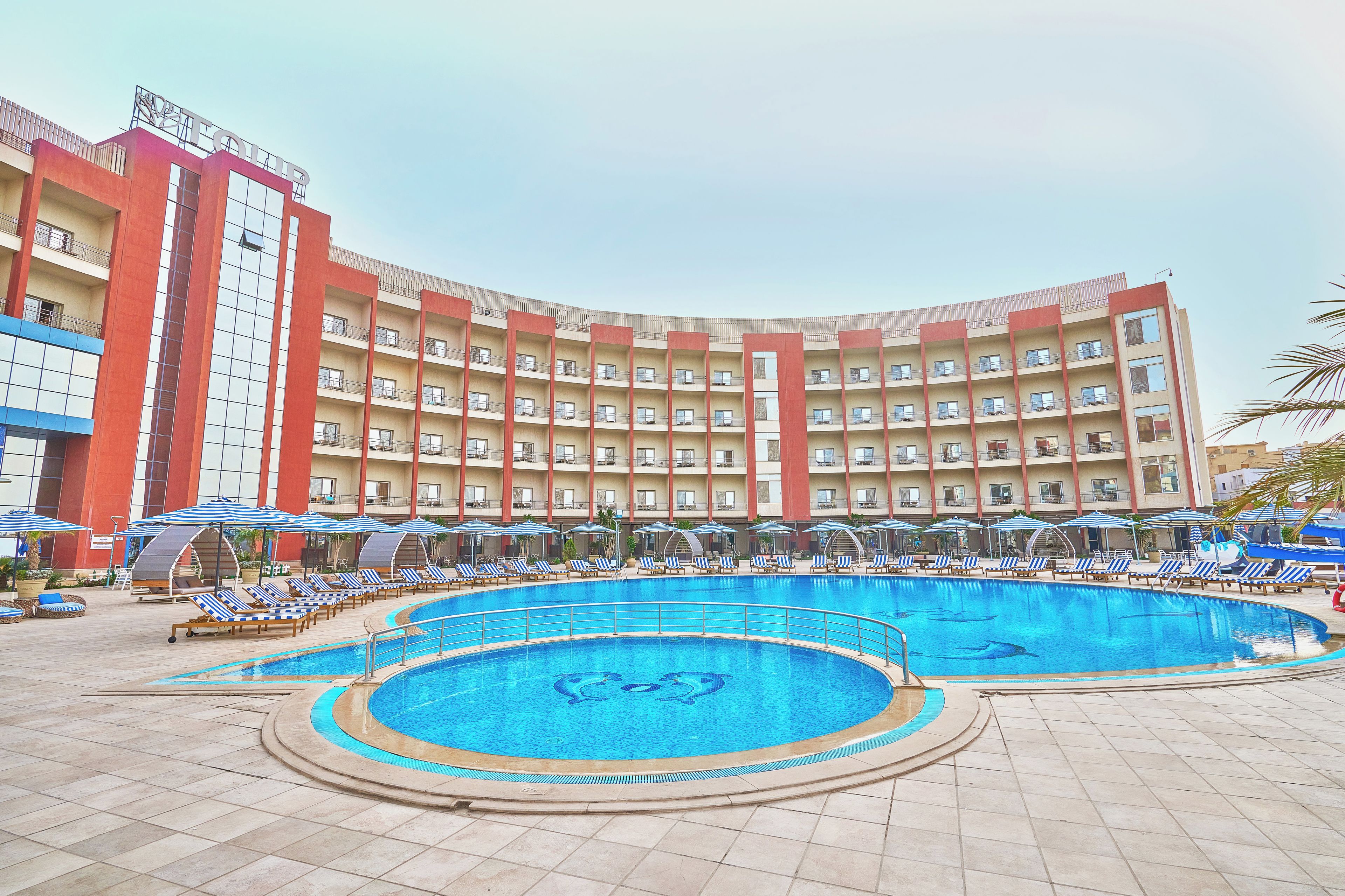 Un hotel con una piscina amplia, varios balcones y sillas de descanso.