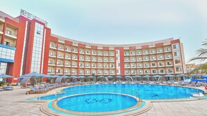 Un hotel con una piscina amplia, varios balcones y sillas de descanso.