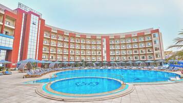 Un hotel con una piscina amplia, varios balcones y sillas de descanso.