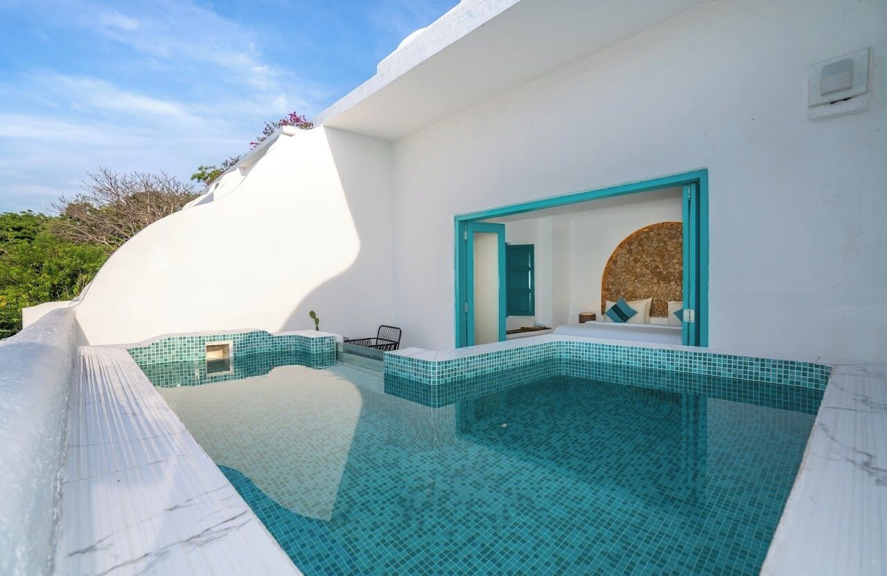 A modern pool area with a white exterior, a blue-tiled infinity edge, and a doorway leading to a room with a circular window.