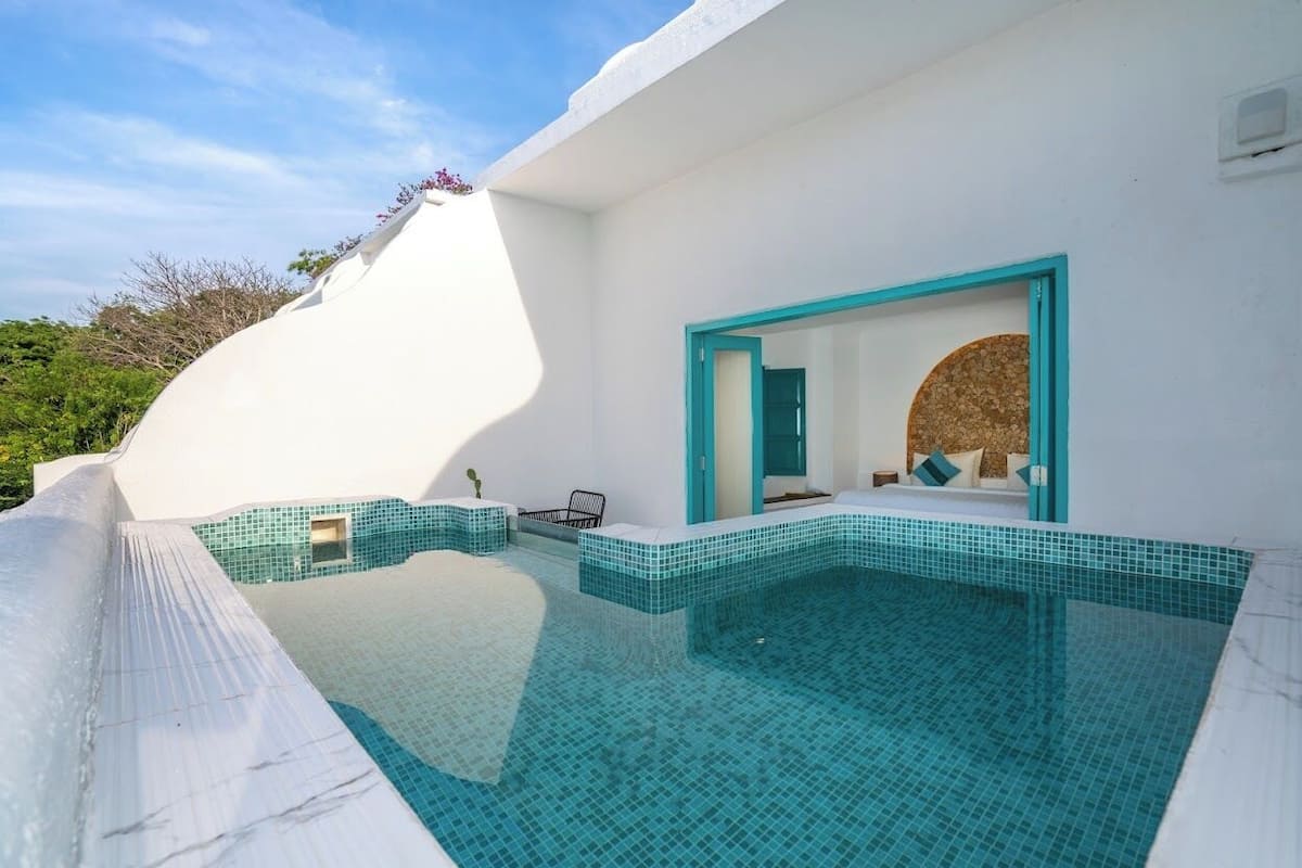 A modern pool area with a white exterior, a blue-tiled infinity edge, and a doorway leading to a room with a circular window.
