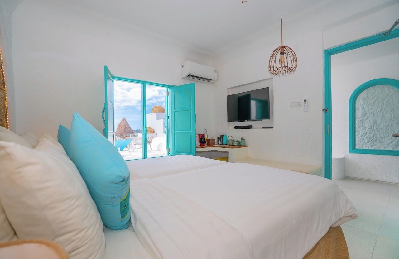A bedroom with a bed, a TV, a desk, and a view of a building with a pyramid-shaped roof.