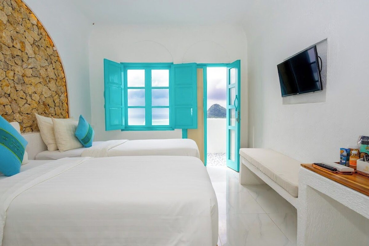 Ein Hotelzimmer mit zwei Betten, einer Steinwand, einem Fernseher und Blick auf das Meer.