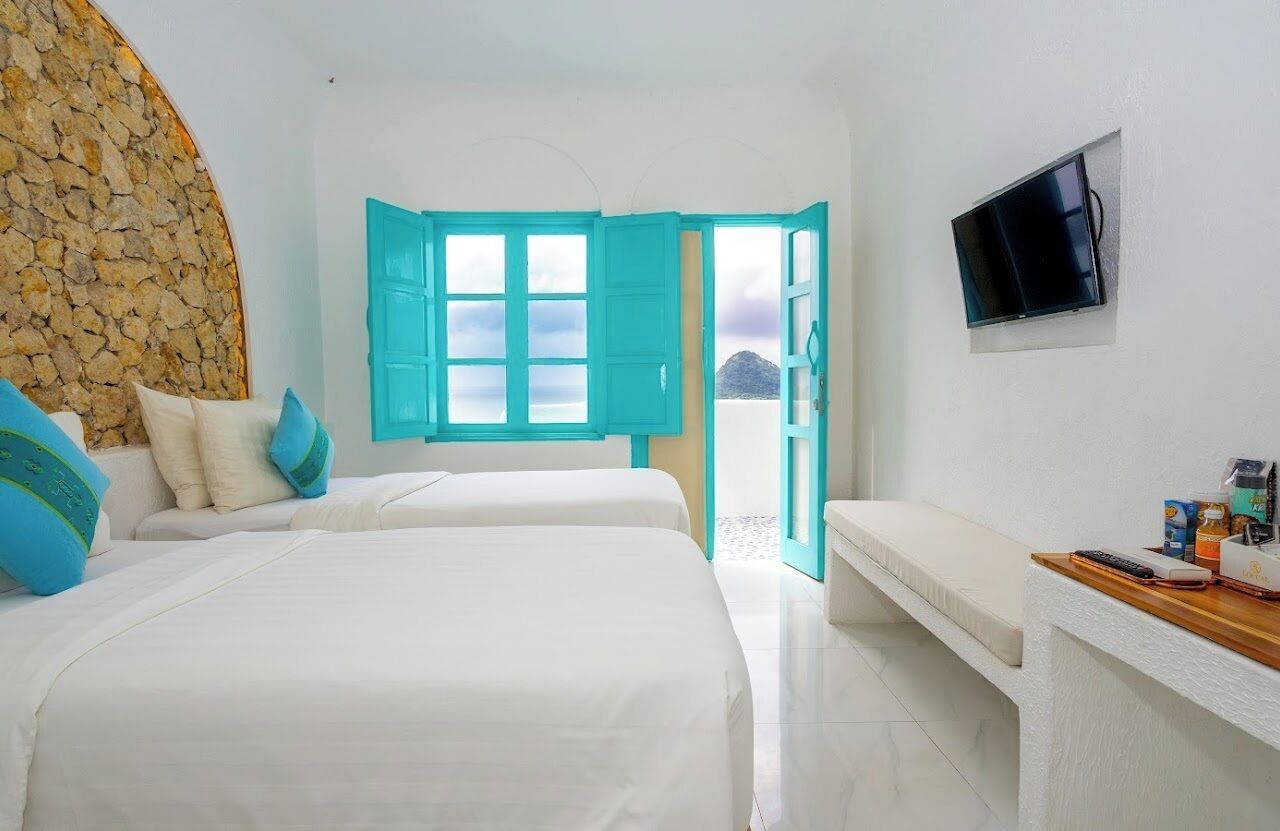 A hotel room with two beds, a stone wall, a TV, and a view of the sea.