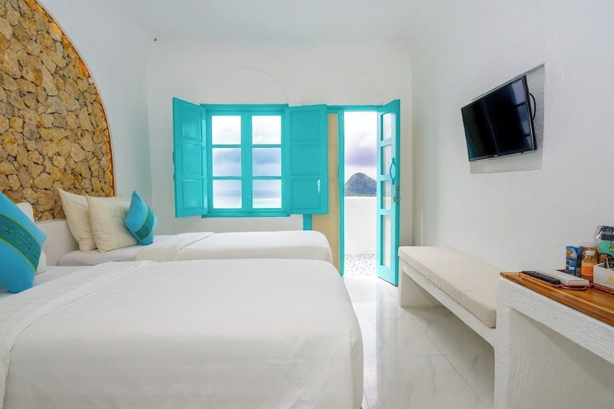 A hotel room with two beds, a stone wall, a TV, and a view of the sea.