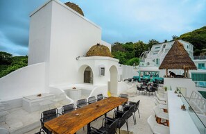 Ein weißes Gebäude mit Holztisch und -stühlen, einem Reetdach und Blick auf das Meer.