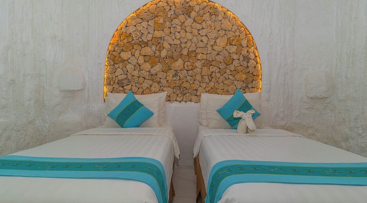 A room with two beds, each with a blue and white bedspread, and a stone wall arch above.