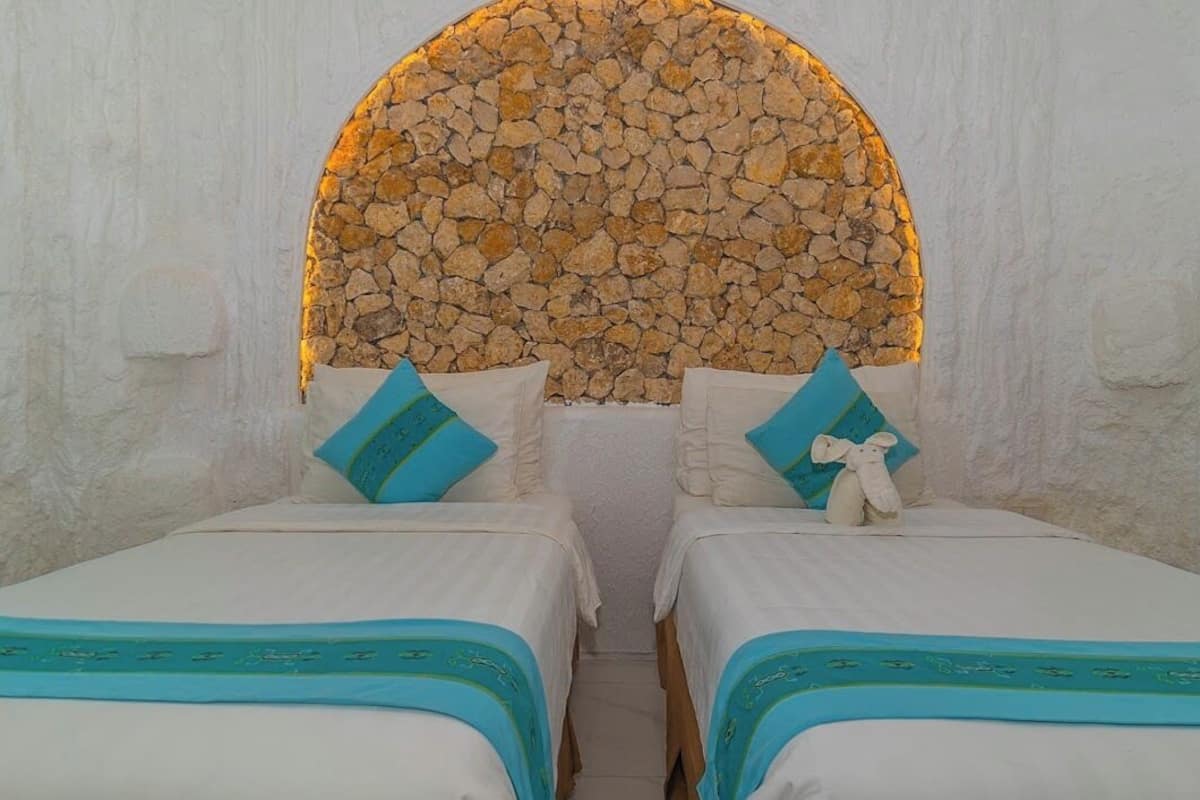 A room with two beds, each with a blue and white bedspread, and a stone wall arch above.