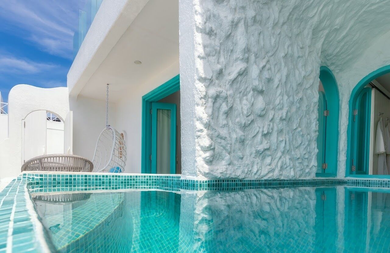 A pool with a clear blue edge, a white textured wall, and turquoise doors.