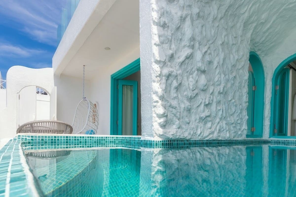 A pool with a clear blue edge, a white textured wall, and turquoise doors.