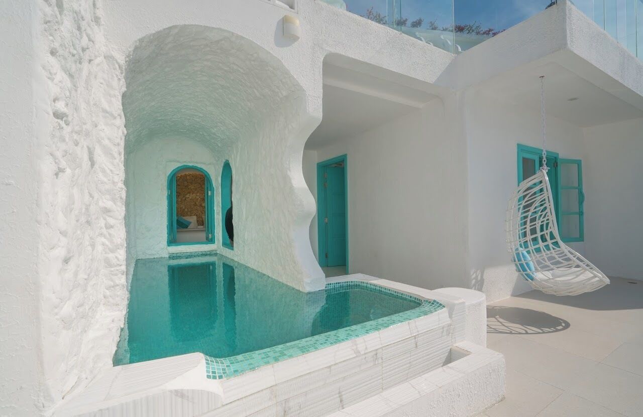 A white-walled building with a swimming pool, a hanging chair, and a door with a blue frame.
