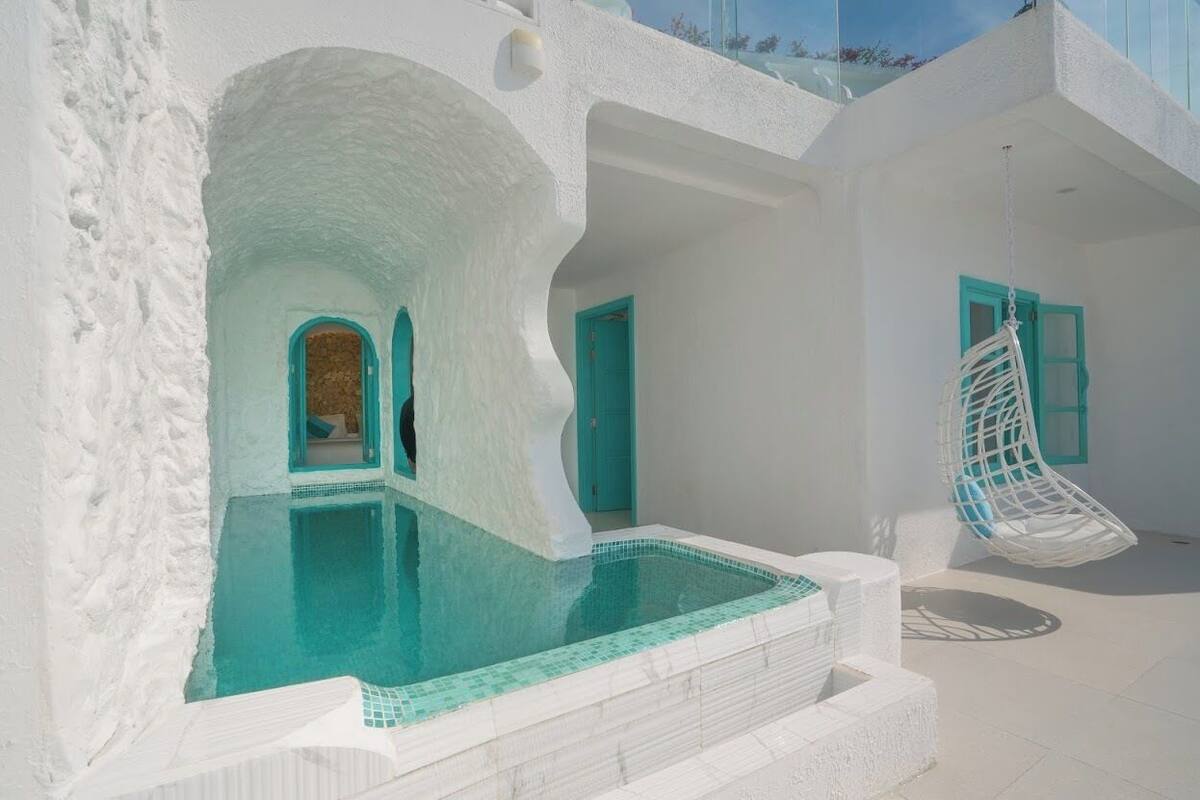 A white-walled building with a swimming pool, a hanging chair, and a door with a blue frame.