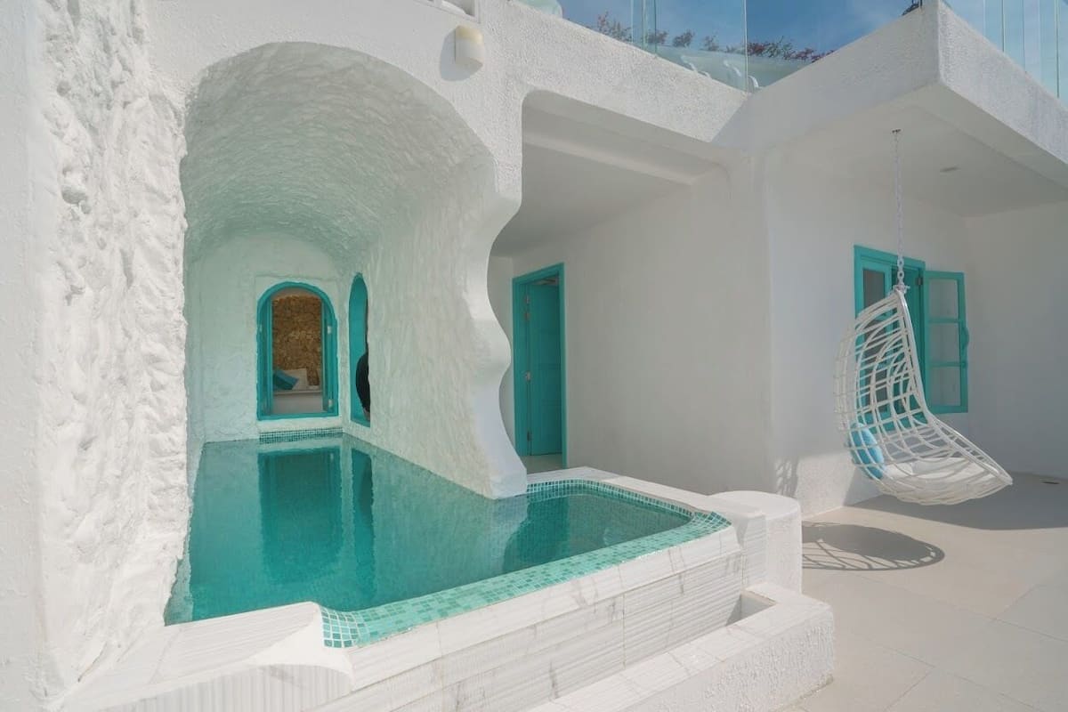 A white-walled building with a swimming pool, a hanging chair, and a door with a blue frame.