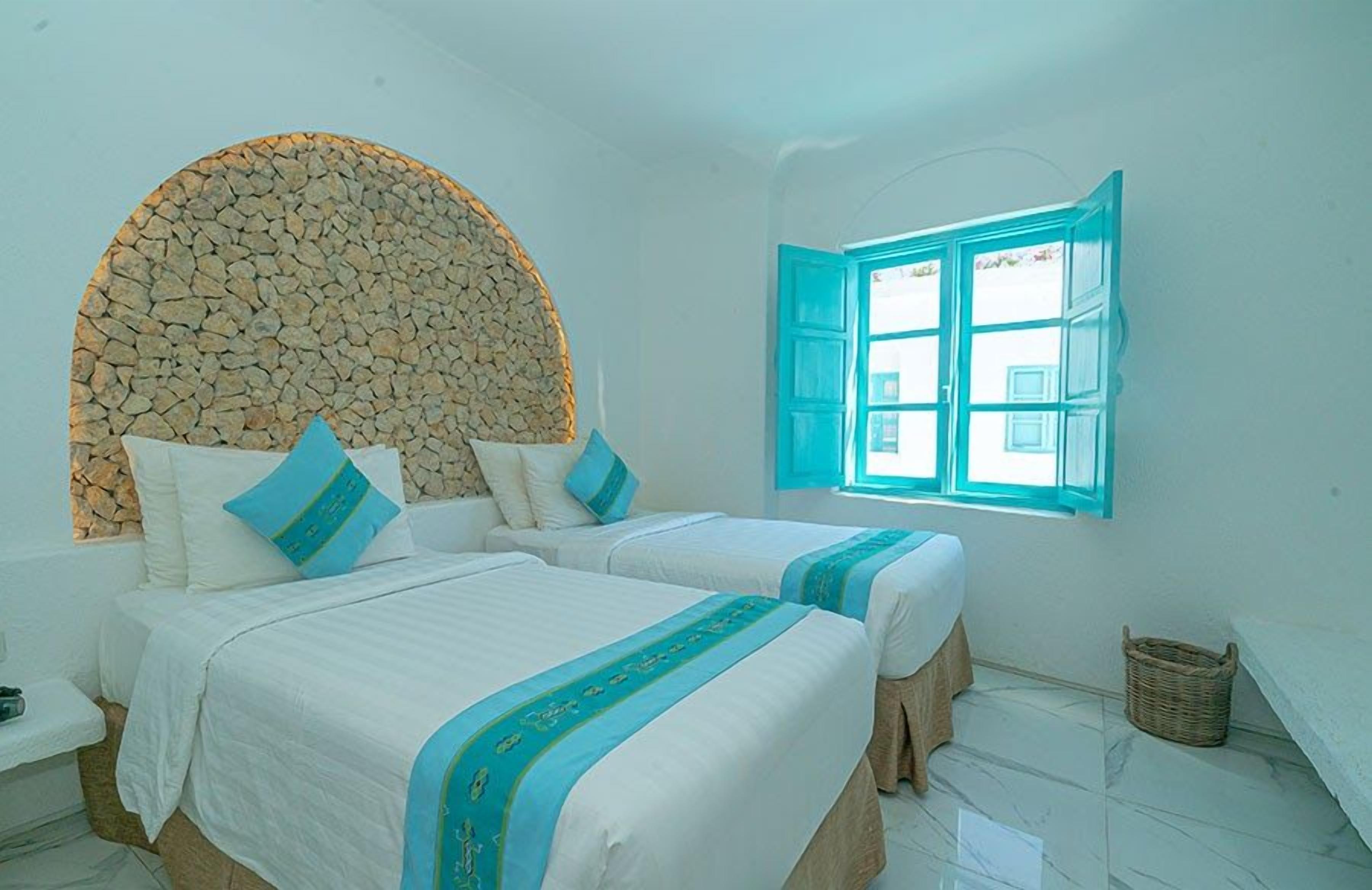 A room with two beds, a stone wall, a window with blue shutters, and a wicker basket.
