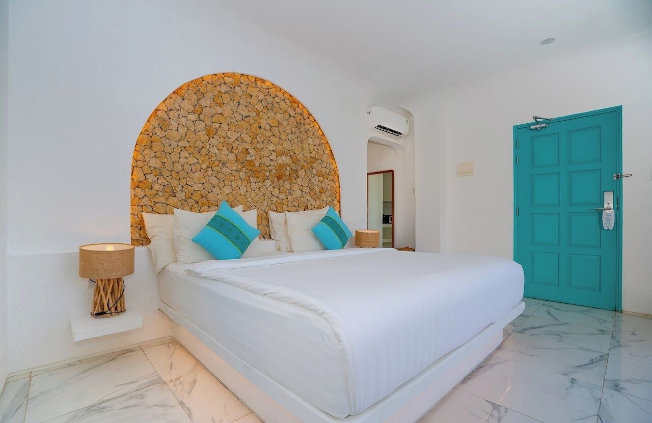 A bedroom with a bed, a circular stone wall, a teal door, and a white lamp.