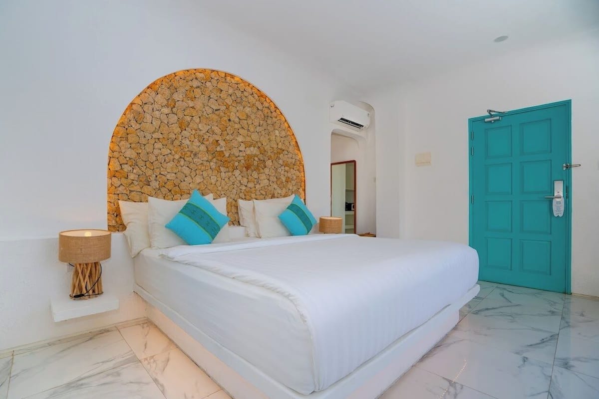 A bedroom with a bed, a circular stone wall, a teal door, and a white lamp.