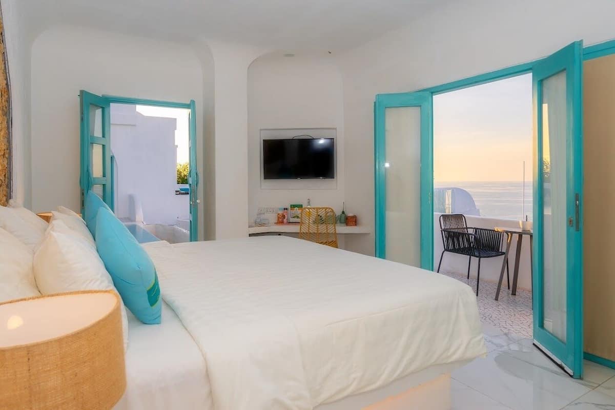 A bedroom with a bed, a television, a desk with a chair, and a balcony with a view.
