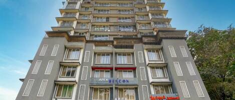 A multi-story building with balconies, a sign reading 'APEX BEACON,' and a storefront with a sign in a foreign language.
