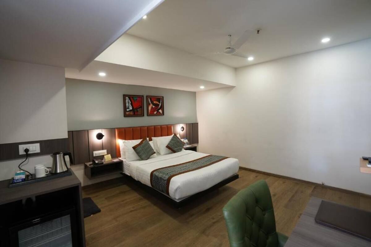A hotel room with a bed, bedside table, lamp, and a desk with a computer.