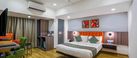 A hotel room with a bed, a desk, a chair, a ceiling fan, and artwork on the wall.