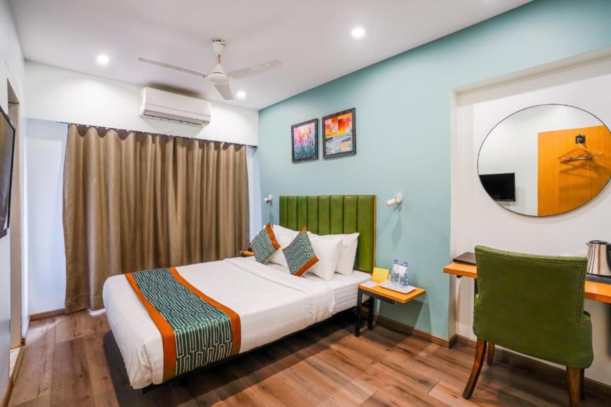 A hotel room with a bed, a desk, a chair, a round mirror, and artwork on the wall.