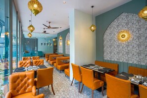 A restaurant with orange upholstered chairs and tables, a patterned wall, and hanging pendant lights. - Apex Beacon Hotel Andheri Mumbai (Mumbai)