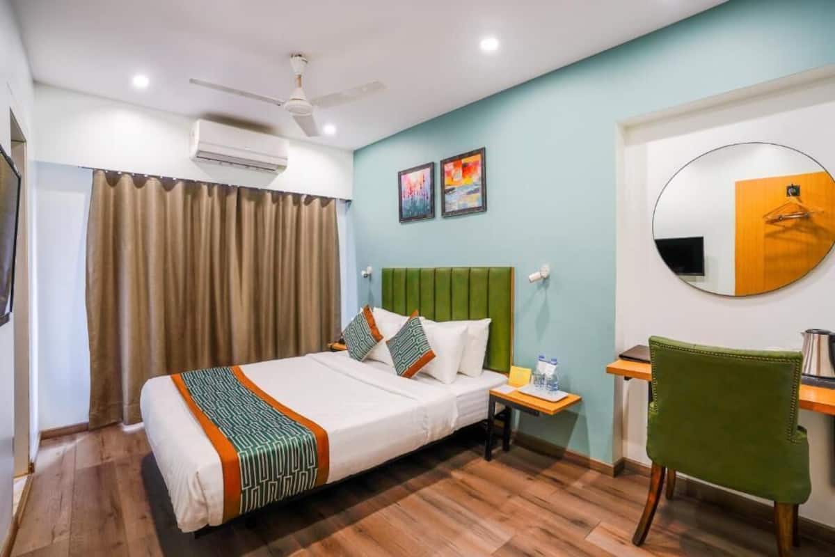 A hotel room with a bed, a desk, a chair, a round mirror, and artwork on the wall.