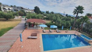 A swimming pool with lounge chairs and umbrellas, a covered seating area, and a view of the surrounding landscape. - Villa Ilios Hotel (Kassandra)