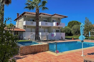 Un edificio de dos pisos con piscina, balcones y una palmera.