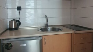 Cocina compacta con armarios de madera, un refrigerador de acero inoxidable, un lavamanos y una estufa.