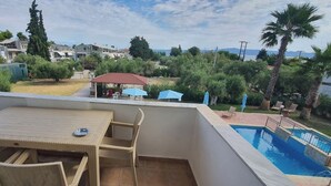 A balcony with a table and chairs, a pool, and a view of a residential area. - Villa Ilios Hotel (Kassandra)