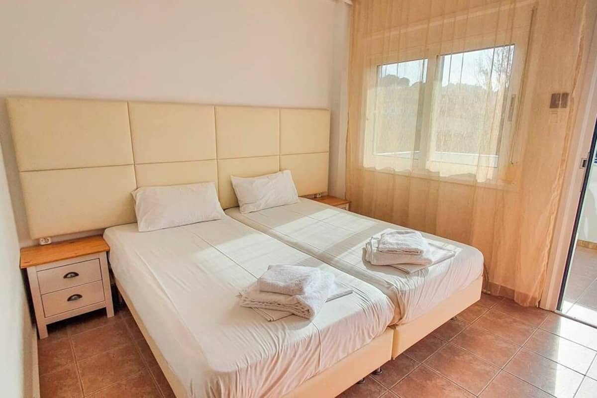 A double bed with a headboard, a nightstand with drawers, and a window with curtains.