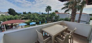 A balcony with wicker furniture, a table, and blue umbrellas. - Villa Ilios Hotel (Kassandra)