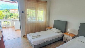 Un dormitorio con dos camas, una ventana con cortinas, un balcón y vistas a edificios y vegetación.