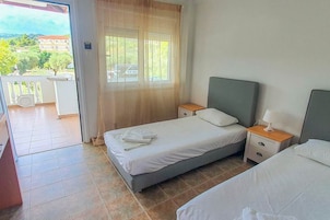 Un dormitorio con dos camas, una ventana con cortinas, un balcón y vistas a edificios y vegetación.