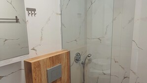 Un baño moderno con pared de mármol, un mueble de madera, un inodoro, un lavabo y cabina de ducha con mampara de vidrio.