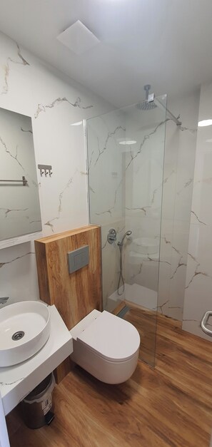 A modern bathroom with a marble wall, a wooden cabinet, a toilet, a sink, and a glass-enclosed shower. - Villa Ilios Hotel (Kassandra)