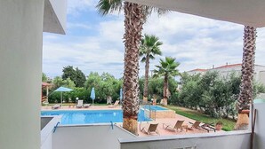 A balcony with a view of a swimming pool, palm trees, and a garden. - Villa Ilios Hotel (Kassandra)