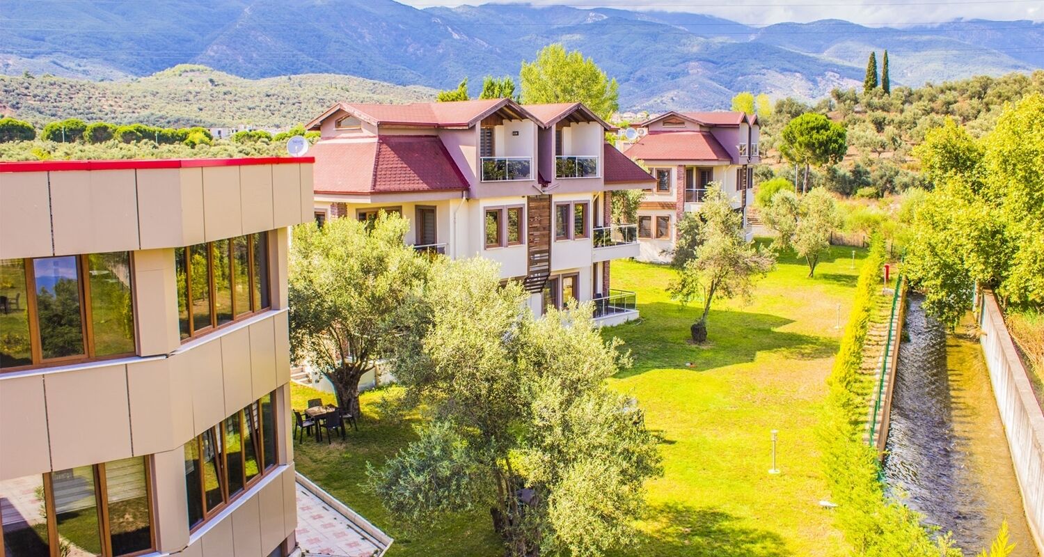 A multi-story hotel with a red roof, surrounded by lush greenery and a view of mountains.