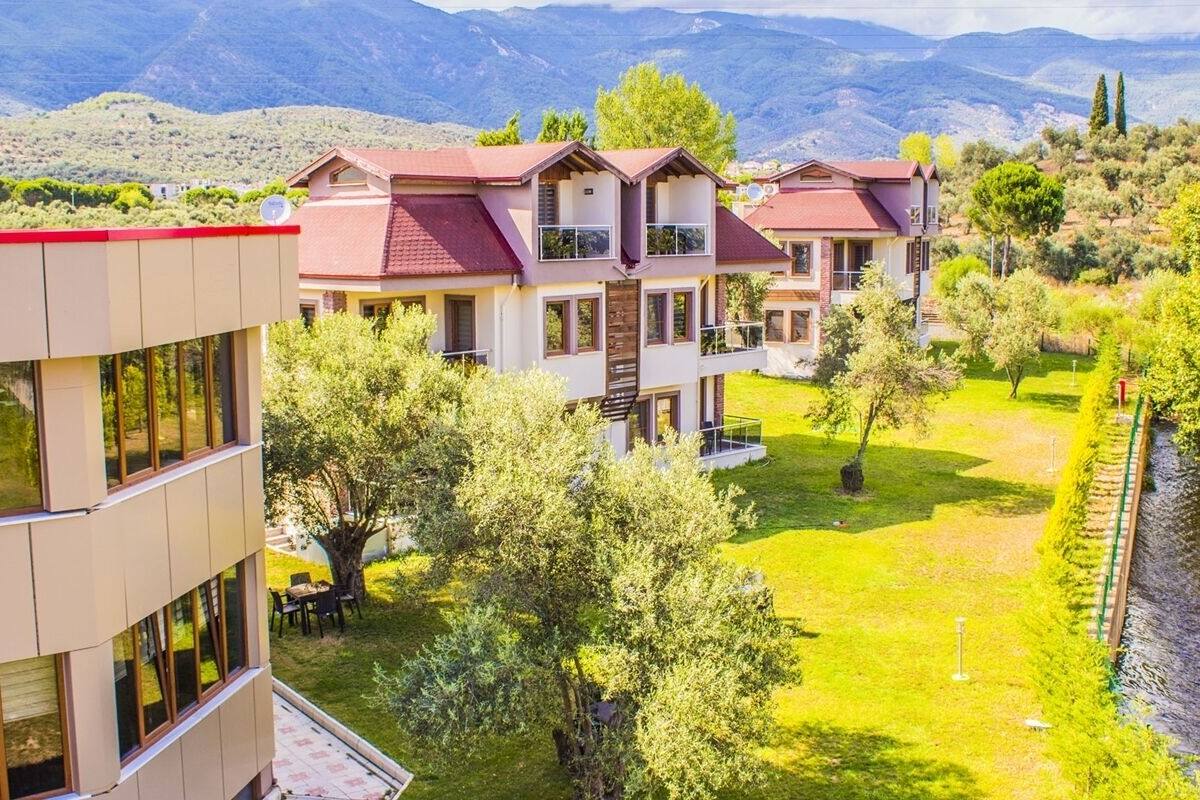 A multi-story hotel with a red roof, surrounded by lush greenery and a view of mountains.