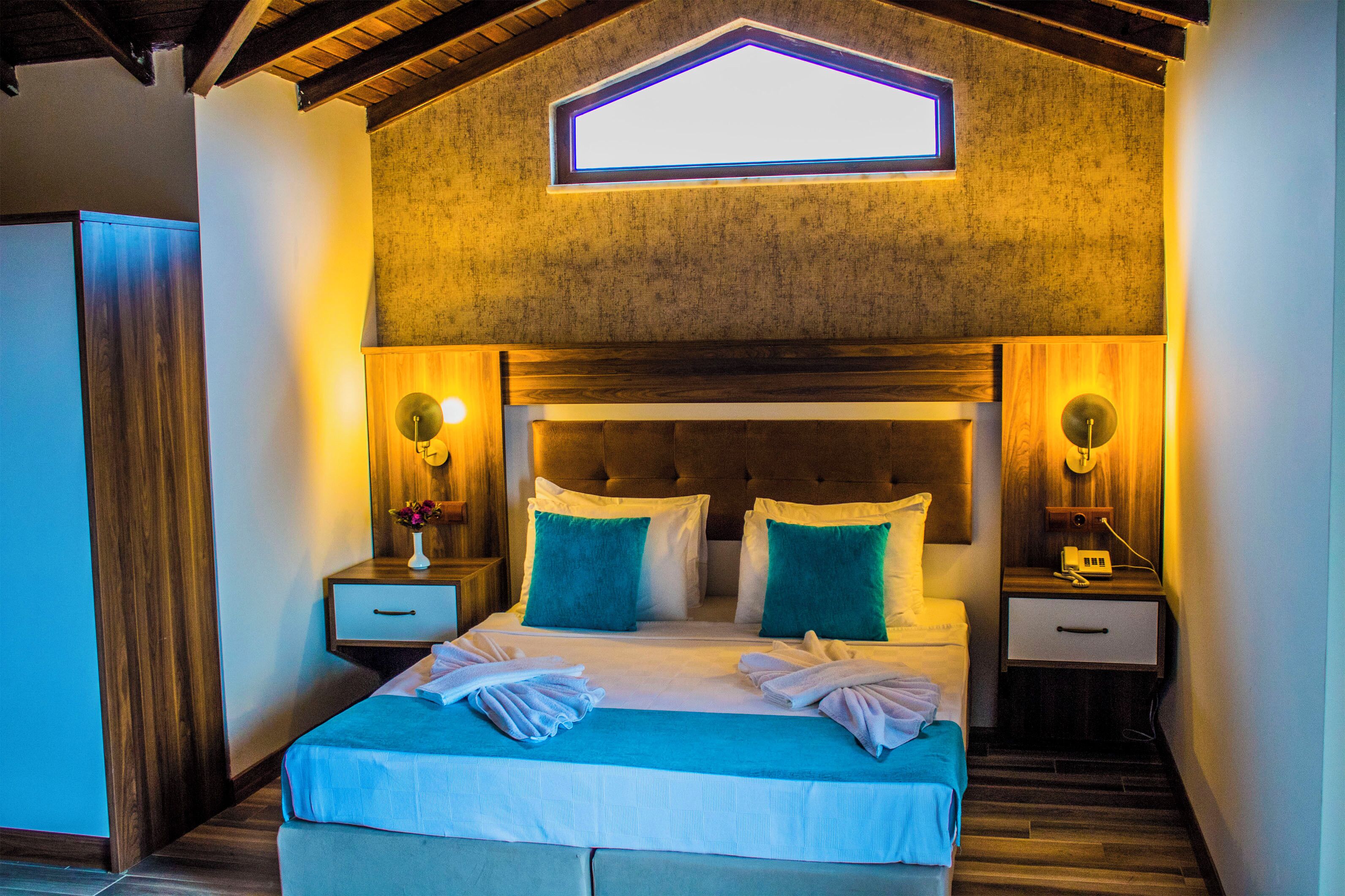 A bedroom with a large bed, two bedside tables, a nightstand, a window, and a wooden ceiling.