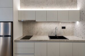 A modern kitchen with a stainless steel refrigerator, two black induction cooktops, a sink, and a built-in range hood. - Lemar (Hersonissos)