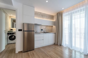 Una cocina moderna con lavadora incorporada, refrigerador de acero inoxidable y un ventanal con cortinas translúcidas.